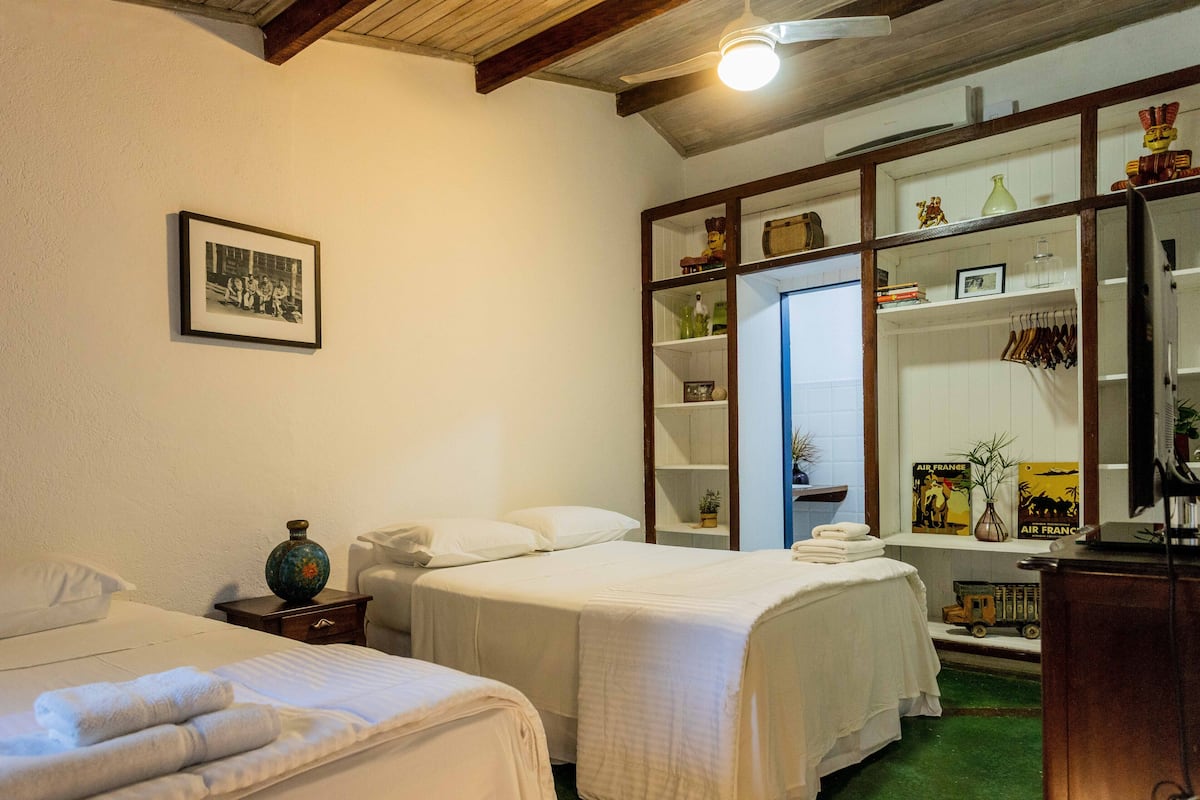 Camera d'albergo con due letti, un armadio, una foto incorniciata appesa al muro e un tavolino con un vaso.