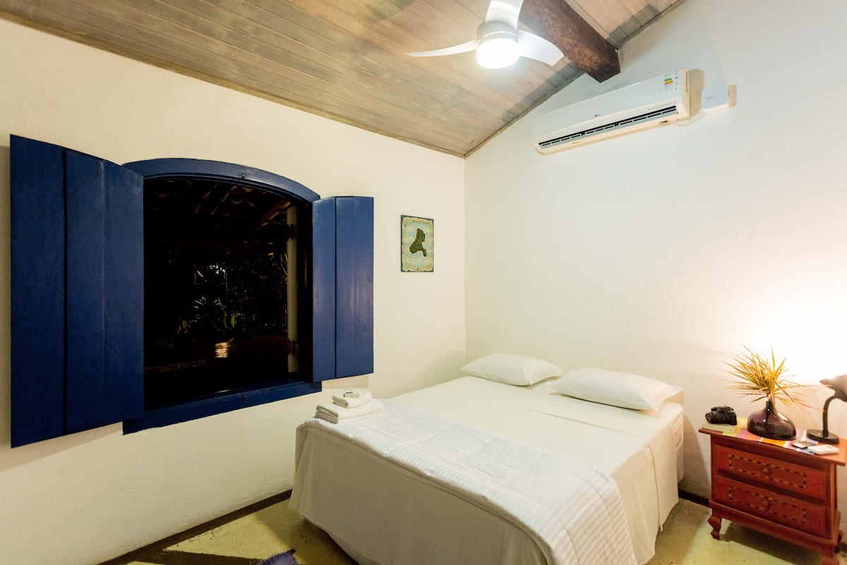 Una camera da letto con un letto, un comodino, un condizionatore d'aria a parete e una finestra con persiane blu.