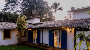 A building with a tiled roof, blue shutters, and a small garden area. - Ilhabela Homestay (Ilhabela)