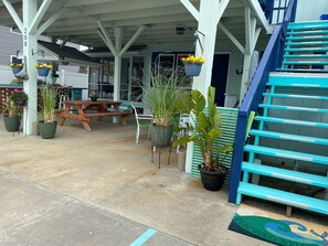 A covered outdoor area with a wooden picnic table, potted plants, and a blue staircase.