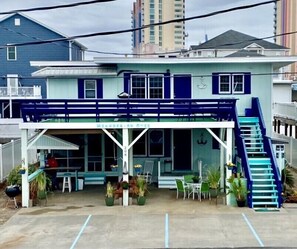 A two-story building with a covered front porch, a staircase, and a small outdoor seating area.