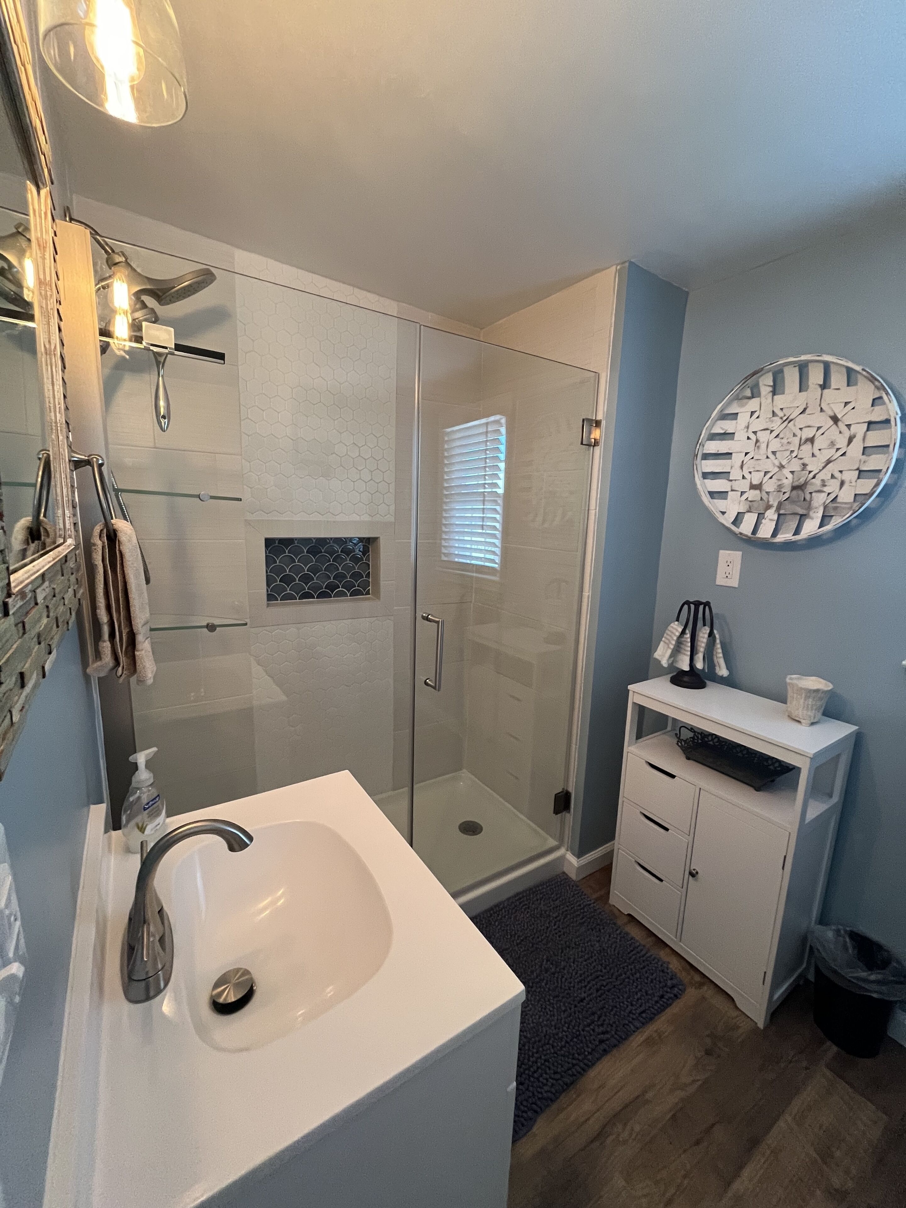 A modern bathroom with a glass shower enclosure, a white sink, and a round mirror.