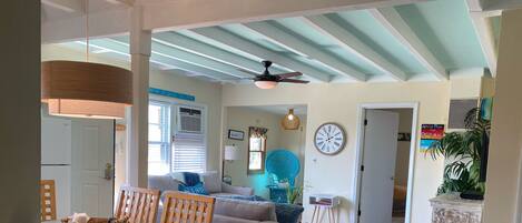 A spacious living room with a dining area, wooden flooring, a ceiling fan, and a clock on the wall.