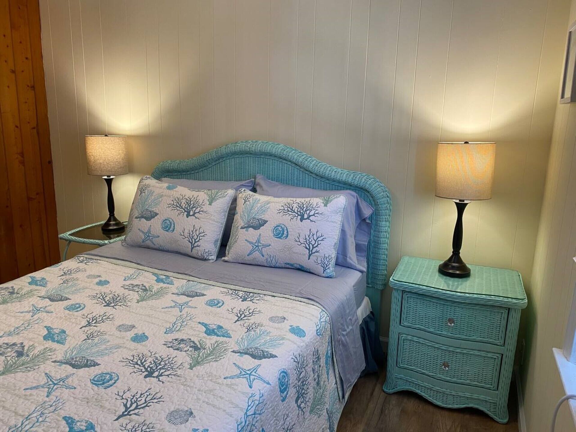 A bed with a blue and white ocean-themed bedspread, flanked by two nightstands with teal lamps.
