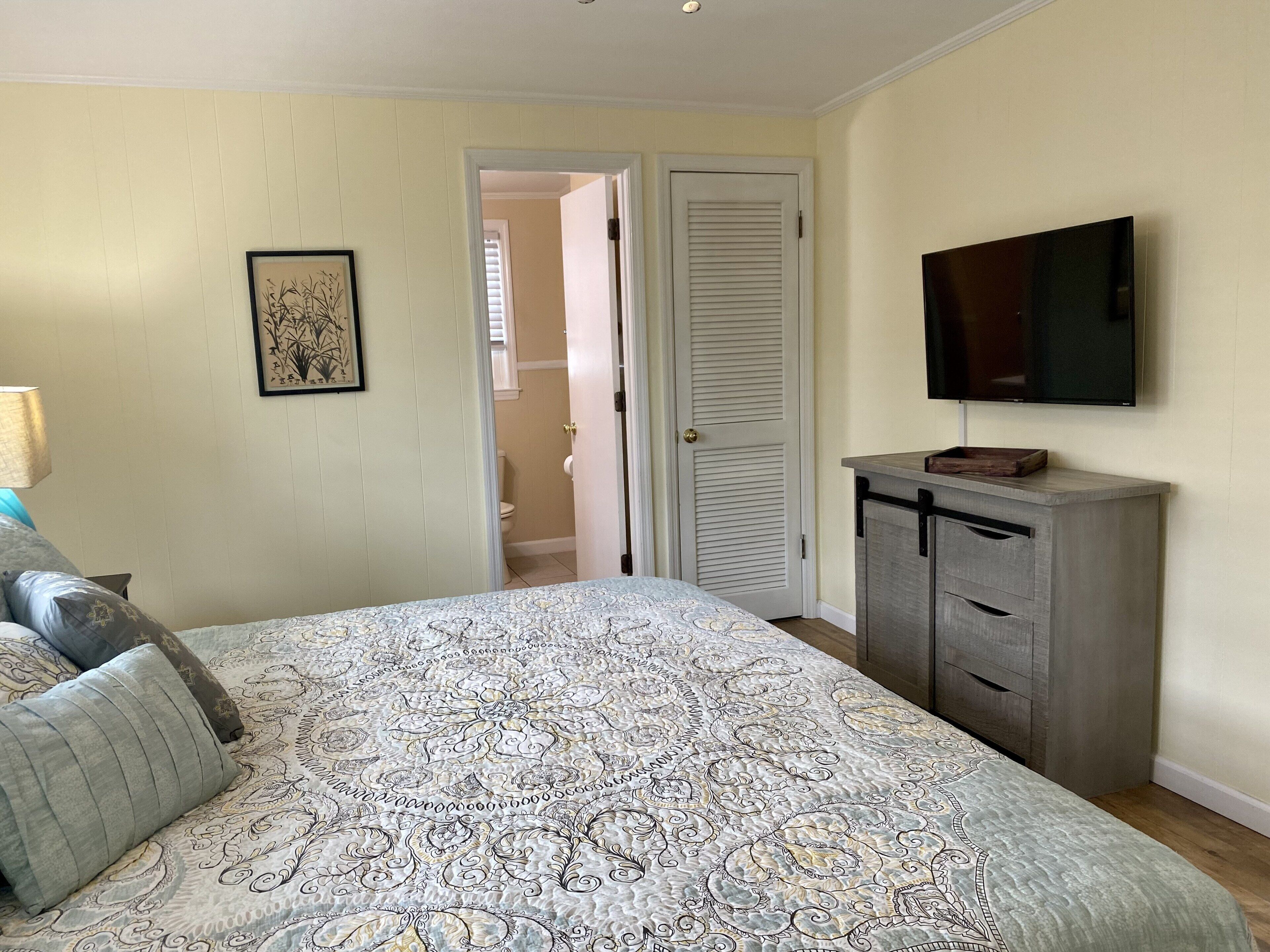 Un dormitorio con cama, cómoda, televisor y puerta que da a otra habitación.
