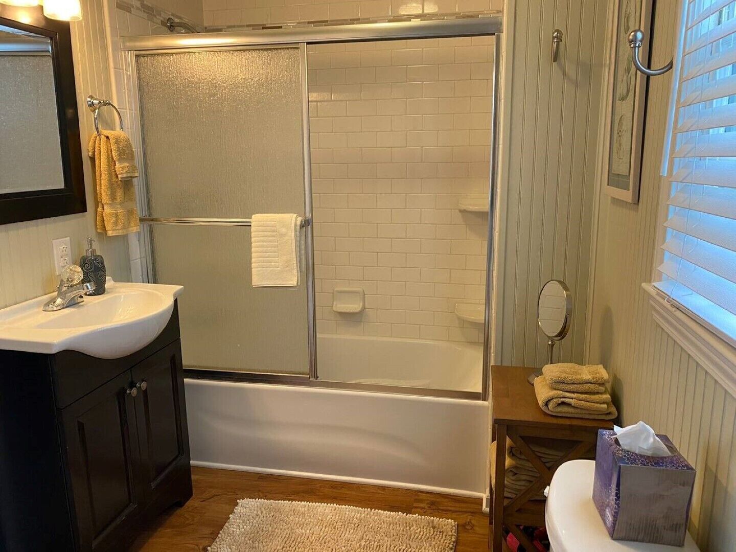 A bathroom with a glass-enclosed shower, a white sink, a toilet, and a small vanity with a mirror.