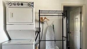Un espace buanderie avec des appareils superposés et un étendoir à linge, sur lequel sont disposés des vêtements et des paniers.