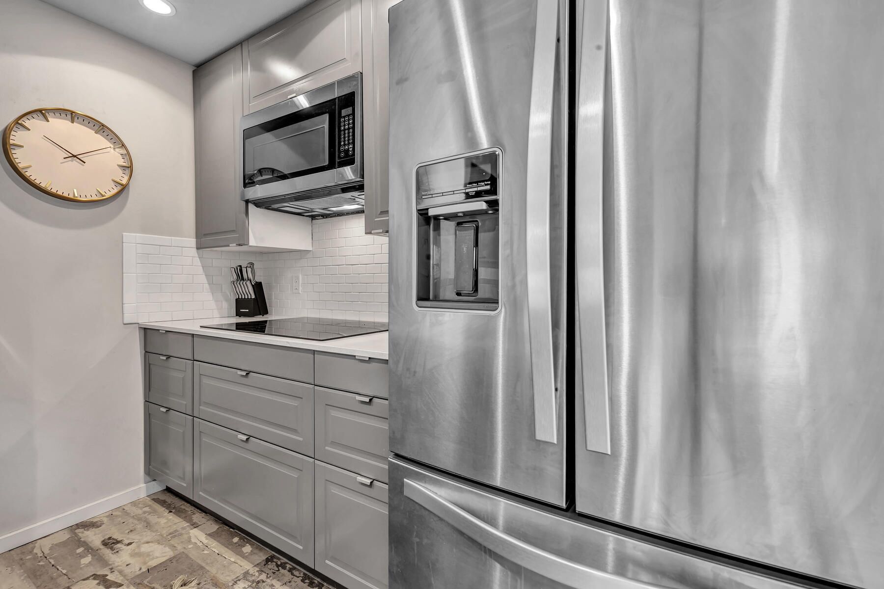 A stainless steel refrigerator with a built-in microwave and water dispenser, a white tiled backsplash, and a wall clock.