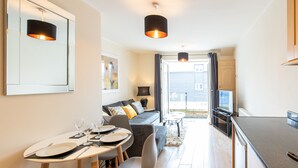 Una sala de estar moderna con sofá, mesa de comedor y una cocina visible a través de una puerta abierta.