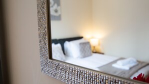 Espejo con marco decorativo que refleja una cama con almohadas y una lámpara de noche.