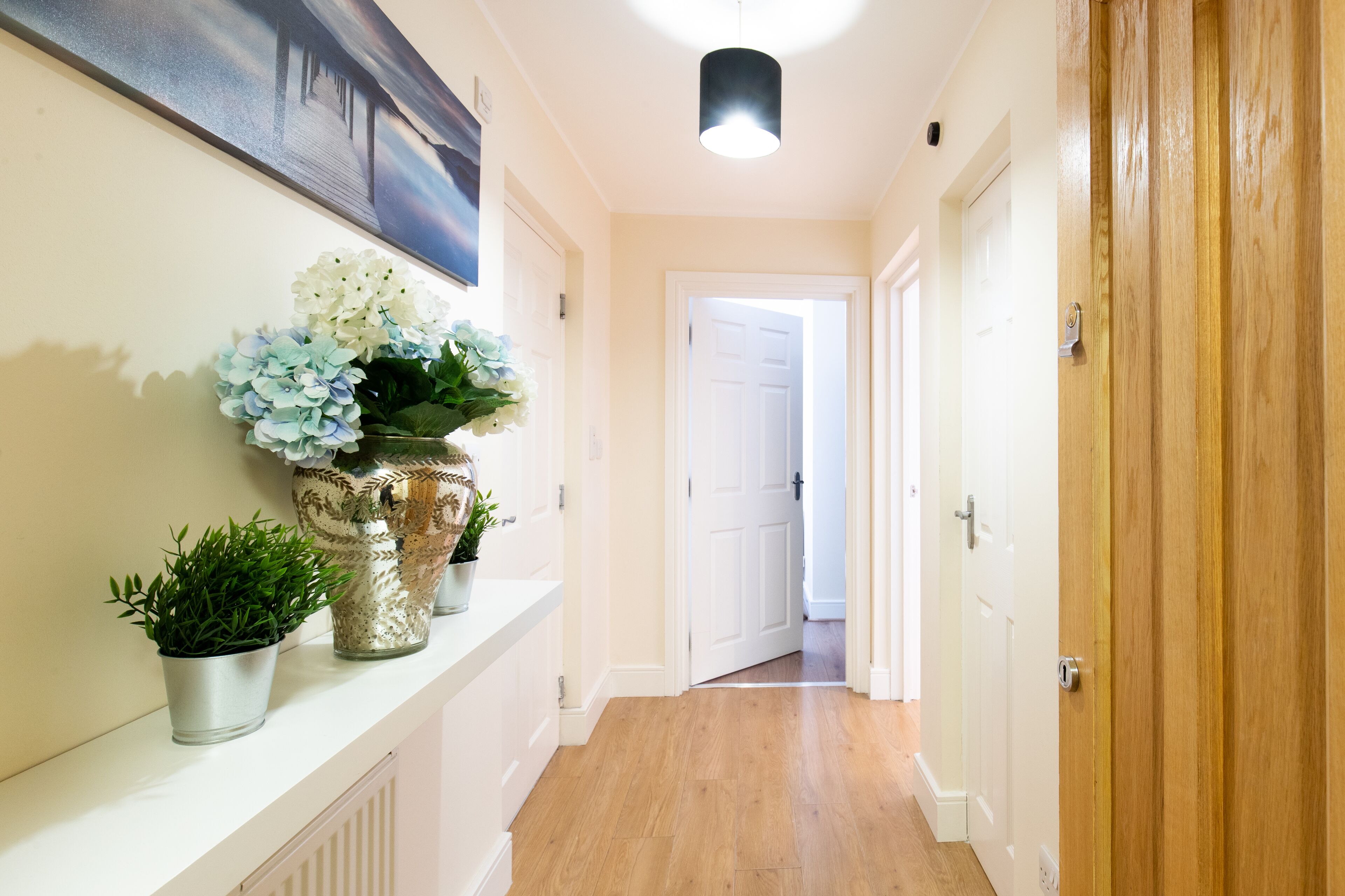 A hallway with a white radiator, a potted plant, and a vase of flowers on a shelf.