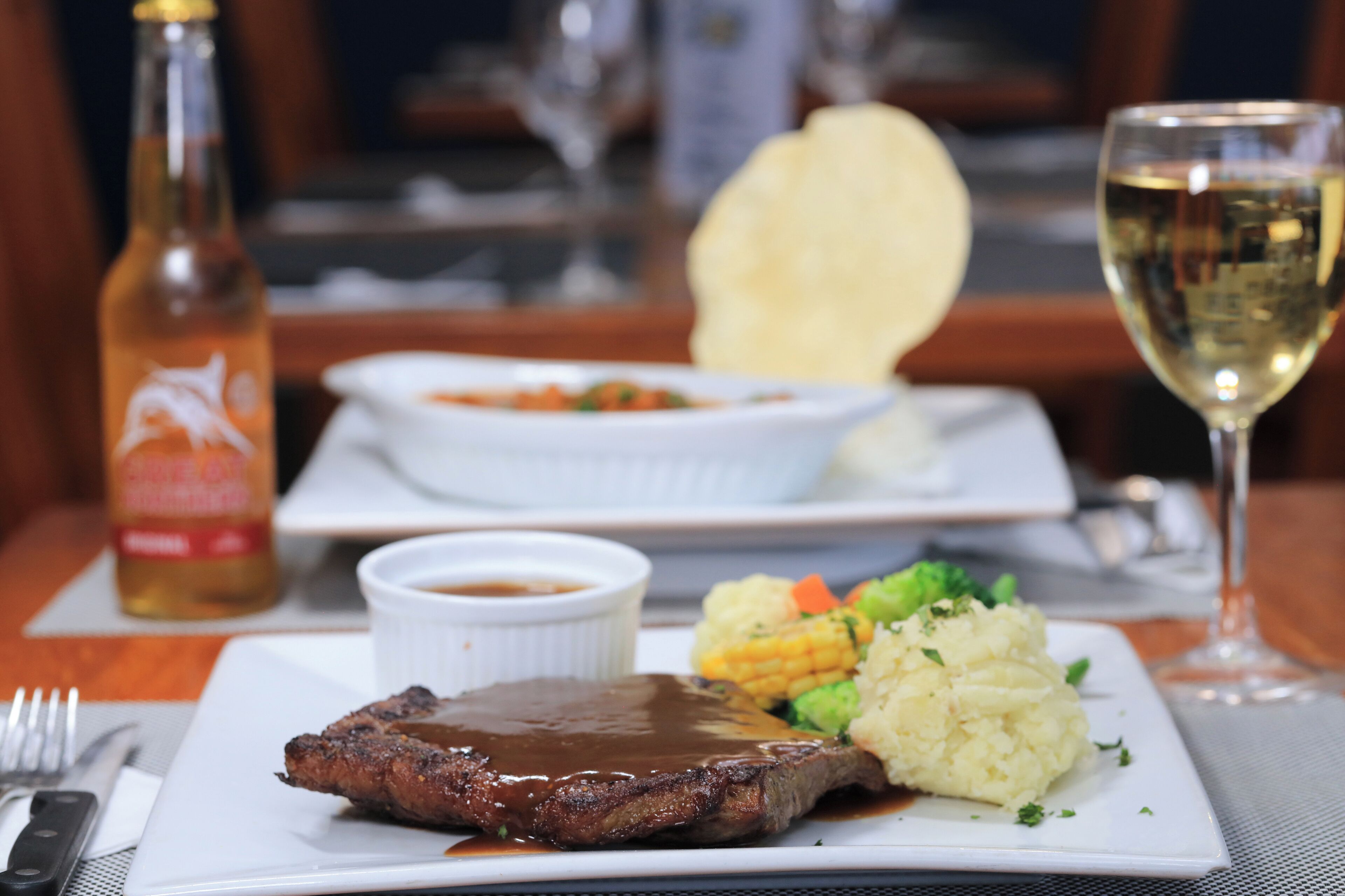 A plate with steak, mashed potatoes, corn, and a small bowl of sauce.