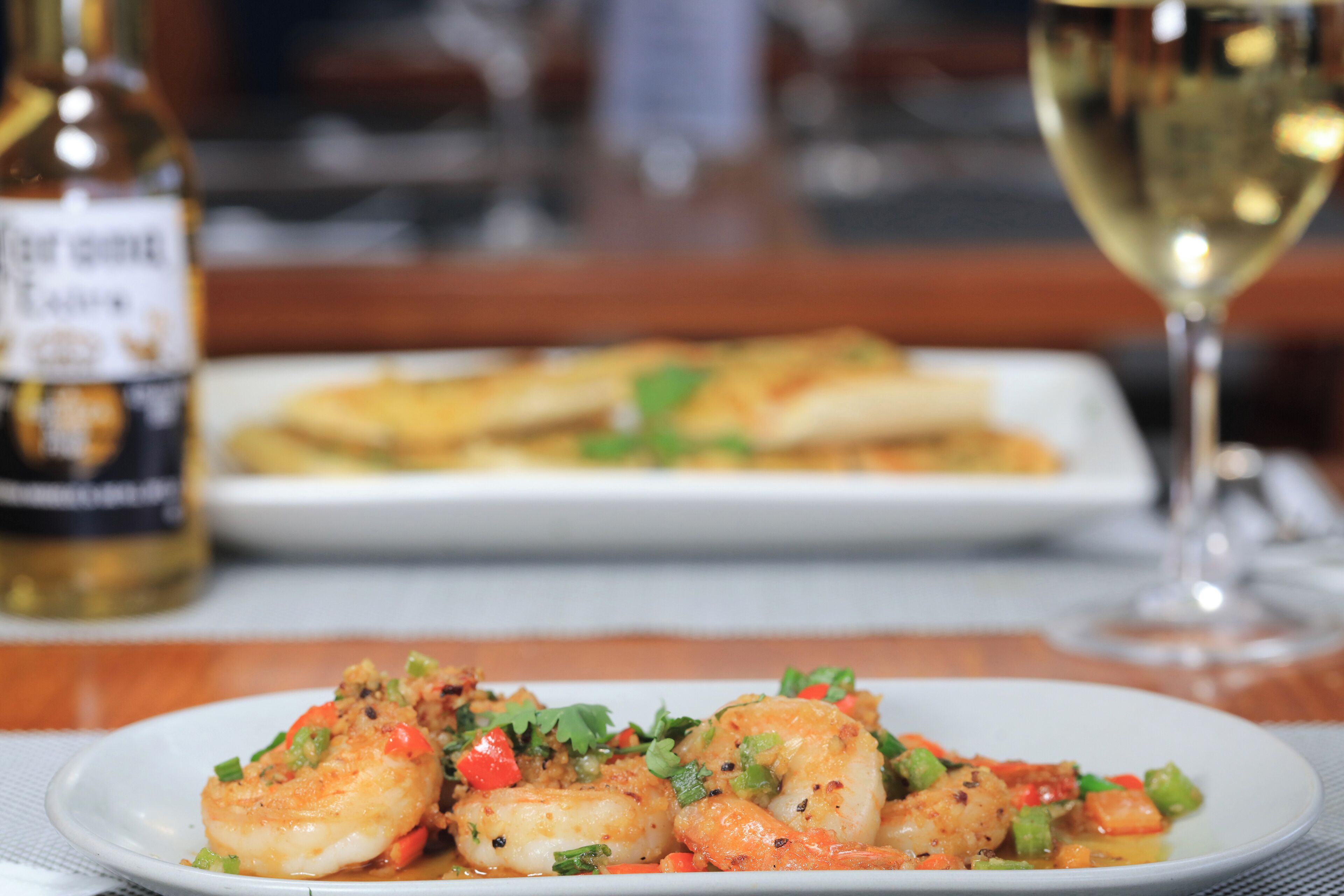 A plate of shrimp with vegetables and a bottle of wine in the background.