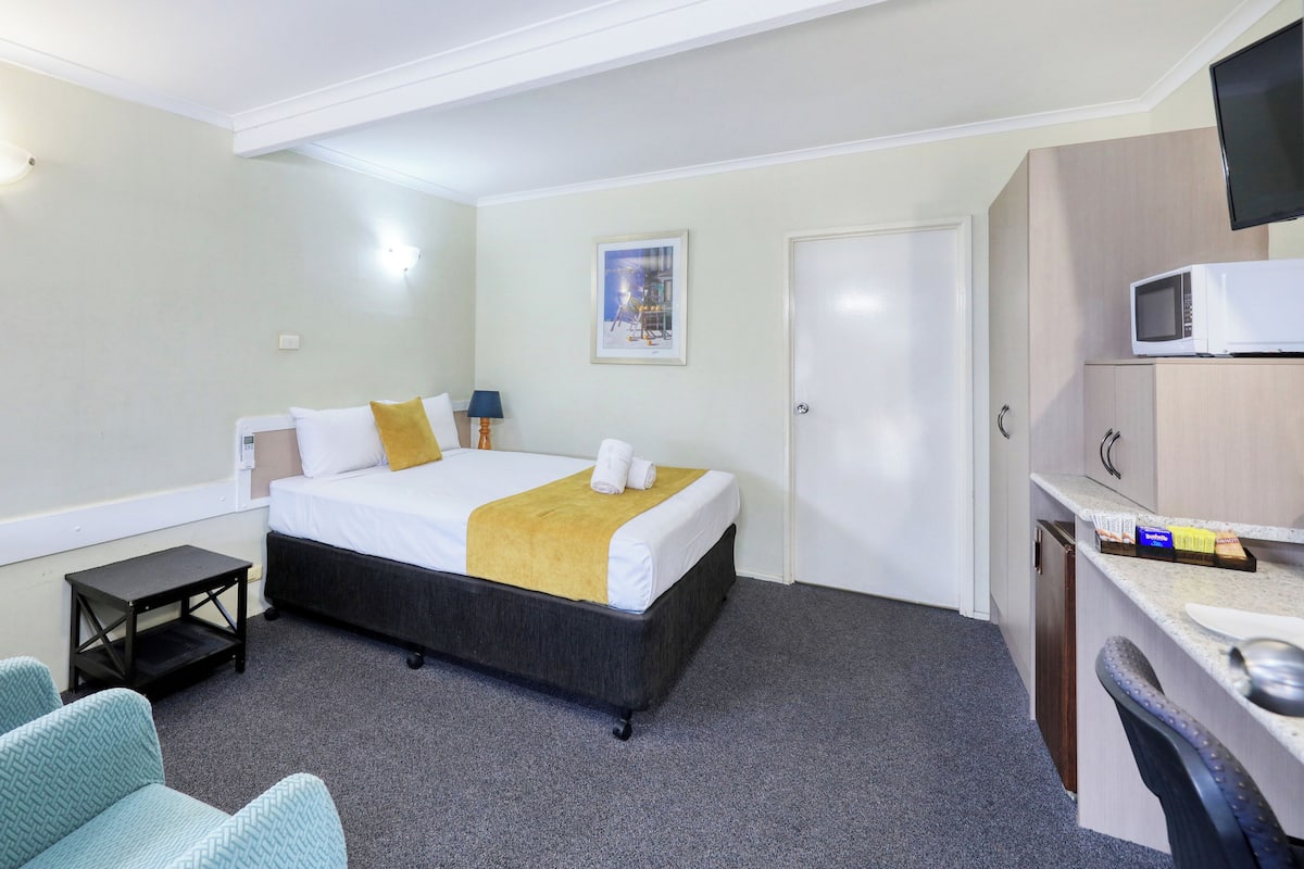 A hotel room with a bed, a desk, a microwave, and a TV.