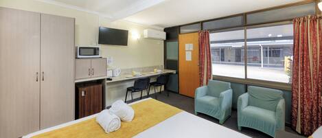A hotel room with a bed, a desk, a microwave, a TV, and two chairs.
