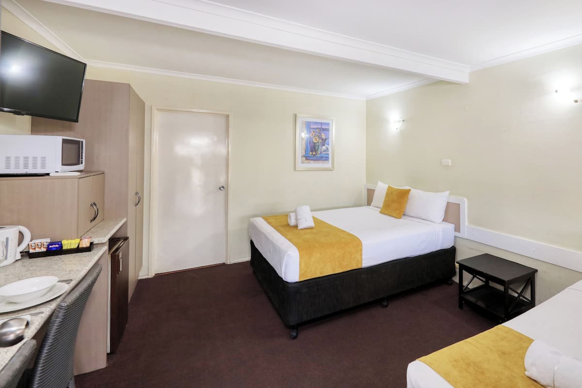 A hotel room with a bed, a bedside table, a TV, a microwave, and a small kitchenette.