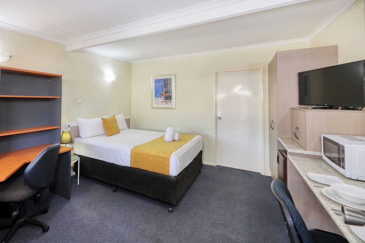 A hotel room with a bed, a desk with a chair, a TV, and a microwave.