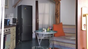 Een kleine kamer met kitchenette, een bed met gestreept beddengoed en een decoratieve tak.