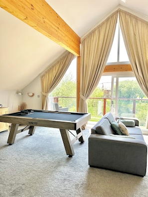 A pool table in a room with a sloped ceiling, a sofa, and large windows with curtains. - Swallow Lodge with Hot Tub, dog friendly sleeps 8, Great resort Facilities! (Winnard's Perch)