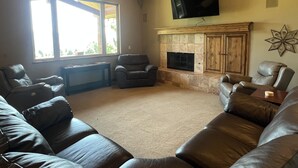 Una sala de estar con sofás de cuero, chimenea, televisor de pantalla plana y un ventanal grande.