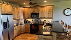 Una cocina con gabinetes de madera, electrodomésticos de acero inoxidable, encimera de granito y un comedor con sillas de madera.