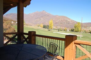 A wooden deck with a metal table and chairs, overlooking a golf course with a mountain in the background. - Turnberry Condo (SSL) (Midway)