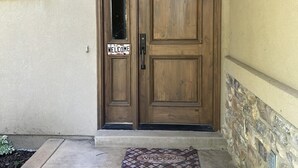 Puertas dobles de madera con un letrero que dice 'WELCOME', un felpudo y una pared de piedra.
