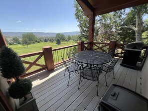 A wooden deck with a round metal table and chairs, a grill, and a view of a green landscape. - Turnberry Condo (SSL) (Midway)