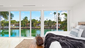 Un dormitorio con un amplio ventanal que da a una masa de agua y palmeras.
