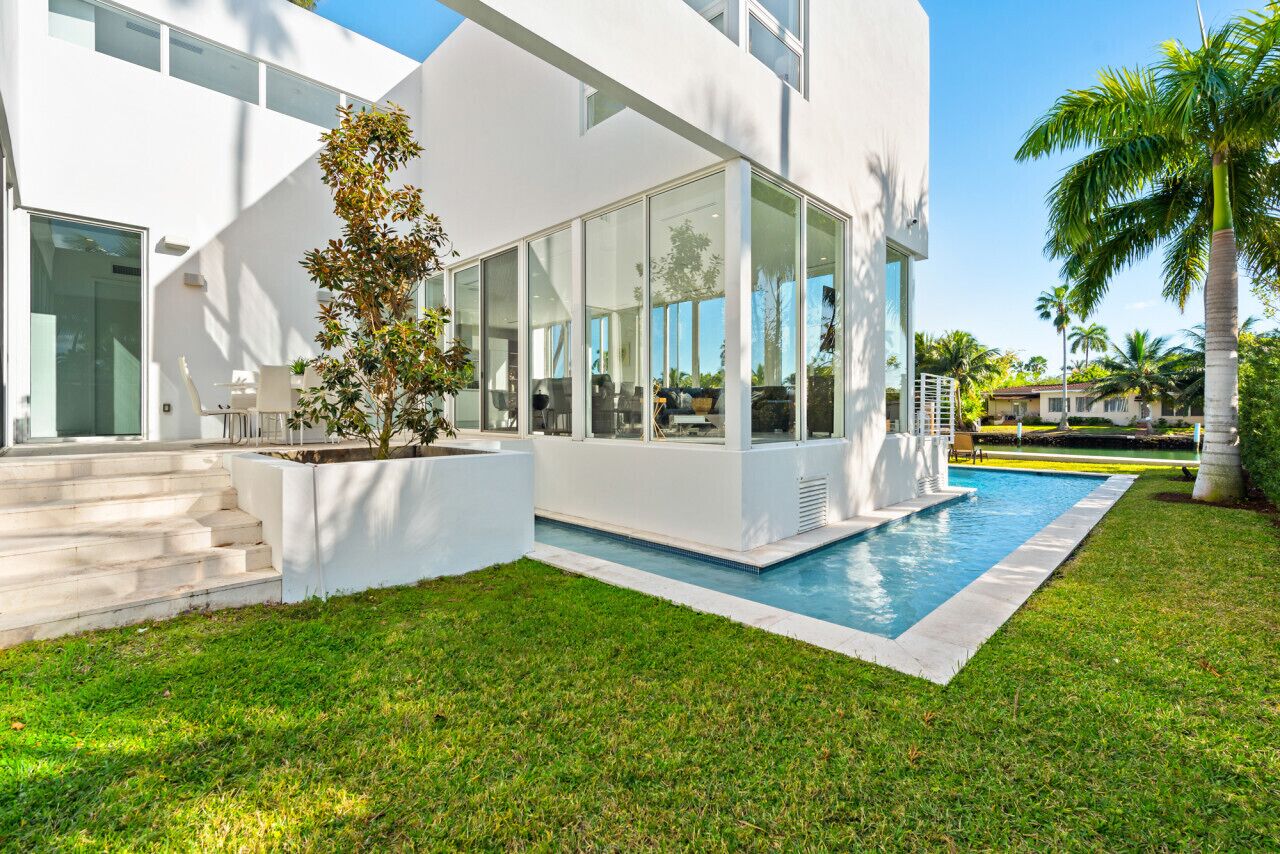 A modern house with a swimming pool, large windows, and a well-maintained lawn.