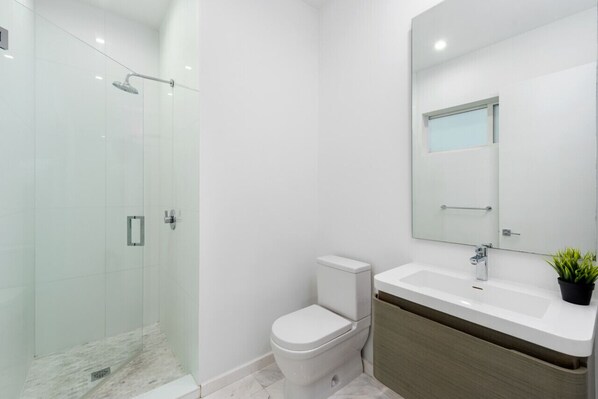 Un baño moderno con ducha de vidrio, inodoro blanco y tocador de madera con lavabo.