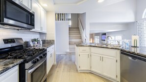 Cozinha moderna com eletrodomésticos de aço inoxidável, armários brancos e bancada de granito.