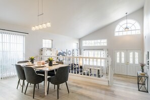 Une salle à manger spacieuse avec un haut plafond, un escalier et de grandes fenêtres.