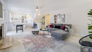 Uma sala de estar moderna com um sofá cinzento, um tapete estampado e um ventilador de teto.