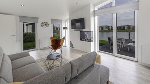 Un salon spacieux avec un grand canapé gris, un fauteuil original et une vue sur un patio aménagé avec du mobilier d’extérieur.
