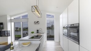 Une cuisine moderne dotée d’un grand îlot central, d’appareils électroménagers intégrés et offrant une vue sur un lac.