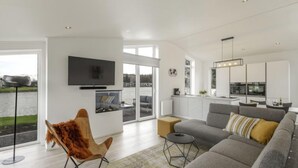 Un salon moderne avec un canapé gris, un fauteuil en fausse fourrure marron et un téléviseur fixé au mur.