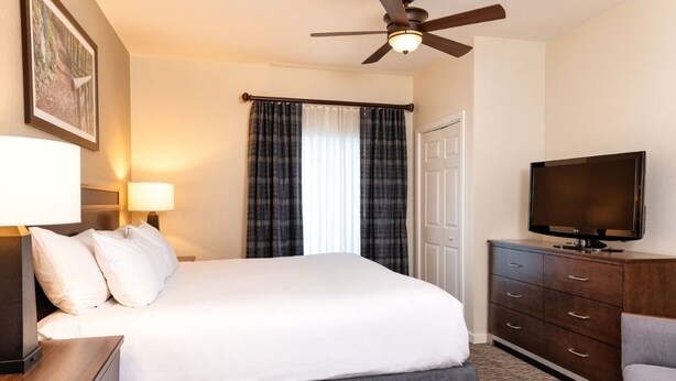 A hotel room with a bed, a television, a desk, and a ceiling fan.