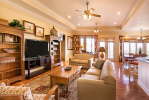 A spacious living room with a flat-screen TV, wooden shelving, a sofa, and a dining area with a chandelier. - Branson | Pool & Mountains | 4BR Sleeps 12 (Banson)