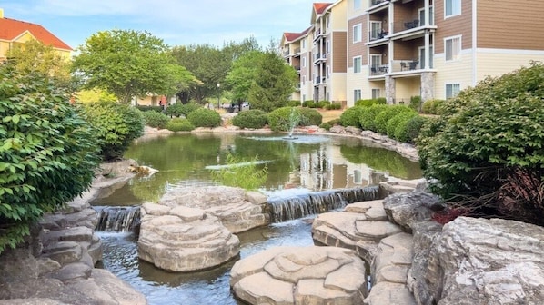 A serene pond with a small waterfall, surrounded by lush greenery and stone formations.