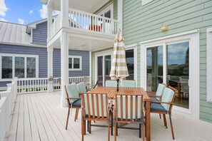 A wooden deck with a table and chairs, a striped umbrella, and a white railing. - Luxurious Sunset Beach Home On The Water With Pool, Boat Dock and Golf Cart (Sunset Beach)