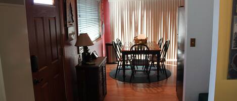 Un comedor con una mesa y sillas de madera, una lámpara y un ventanal con persianas.