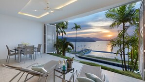 A modern room with a balcony overlooking a sunset view of the sea and boats. - Luxury Apartment Unique Residences (Koh Samui)