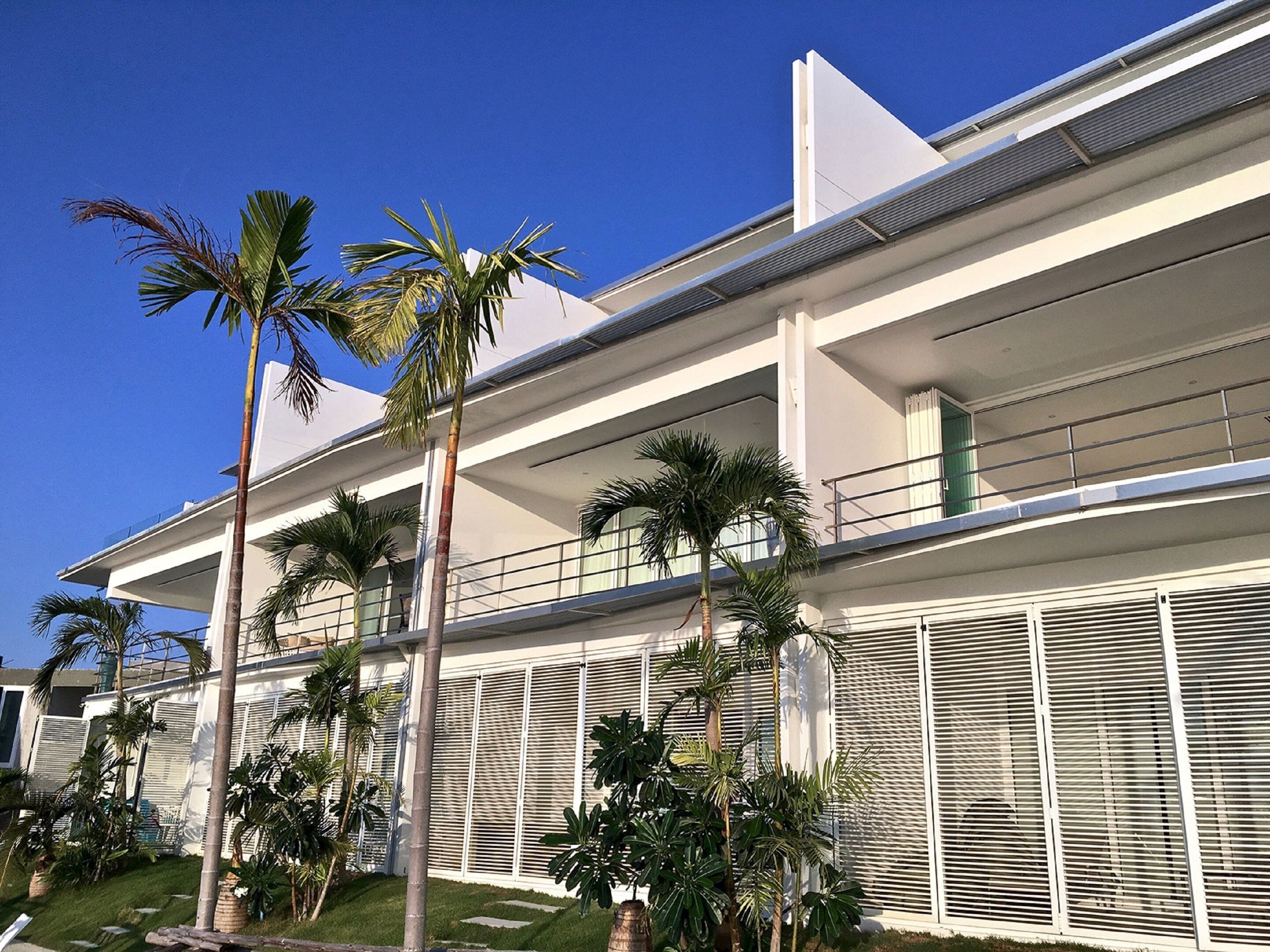 A modern multi-story building with balconies and palm trees.