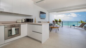 A modern kitchen with a built-in oven and microwave, a dining area with a table and chairs, and a balcony with a view of the ocean. - Luxury Apartment Unique Residences (Koh Samui)