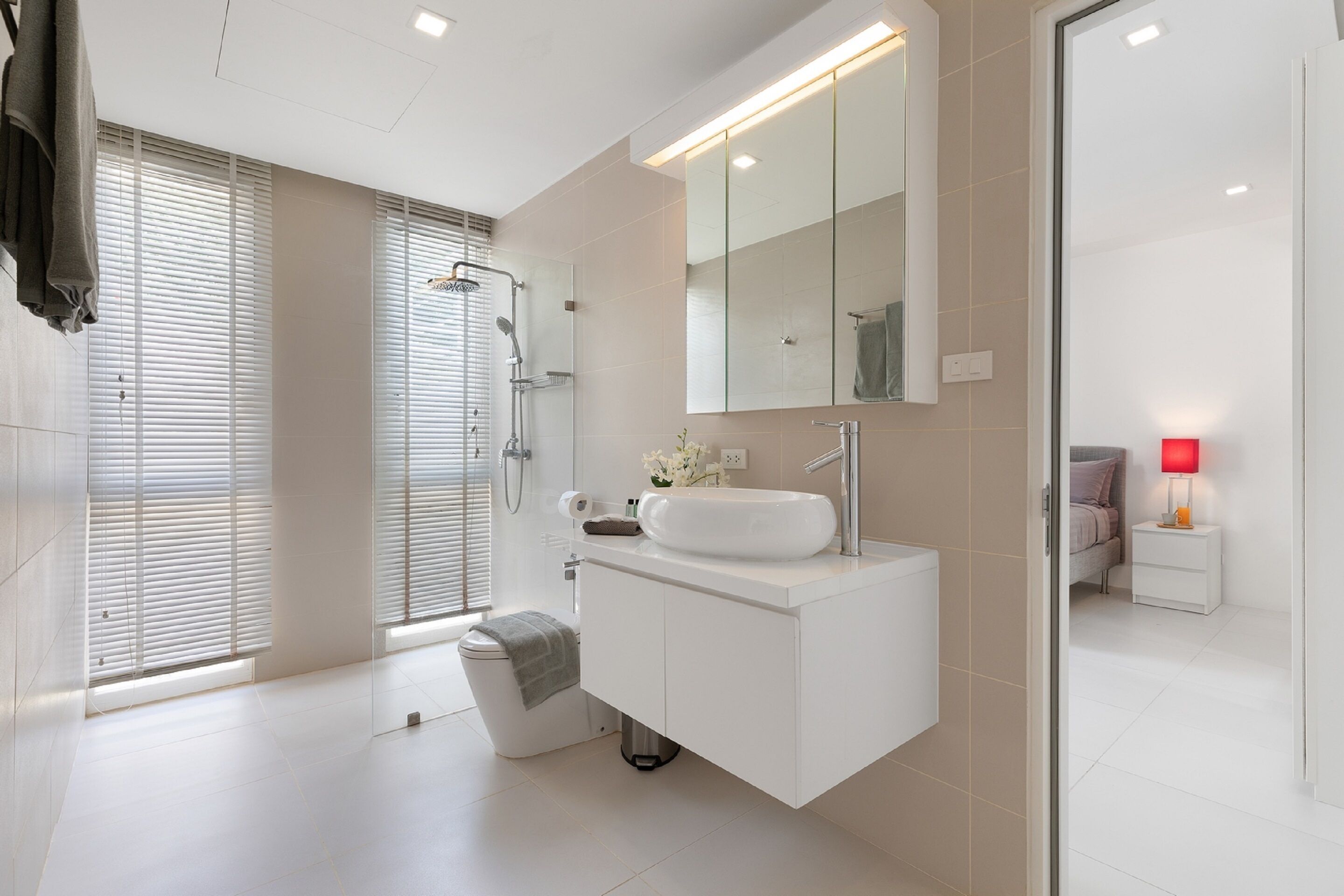 A modern bathroom with a large mirror, white vanity, and a shower area.