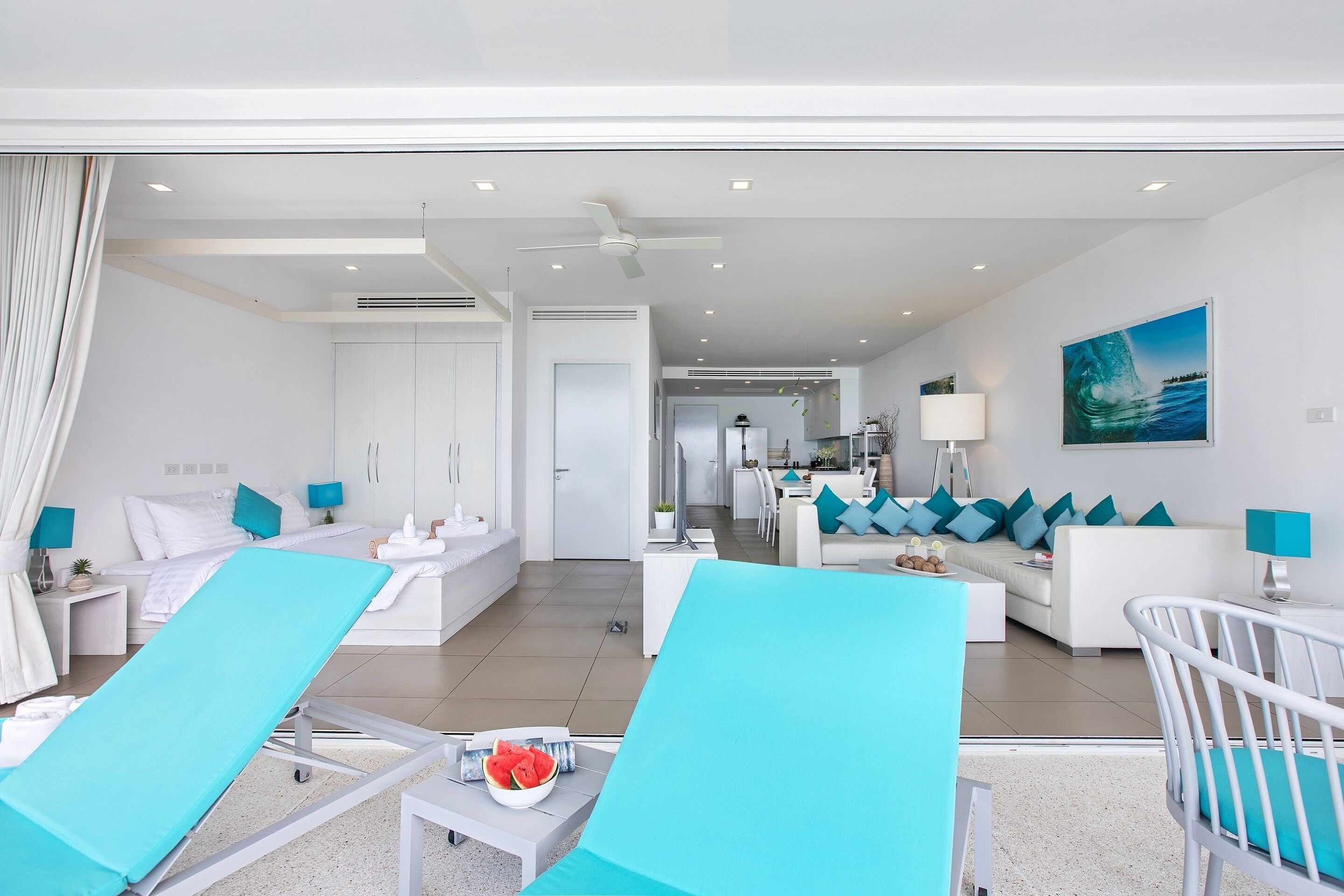 A modern hotel room with a bed, a sitting area with a sofa and chairs, a dining area, and a view of the sea.
