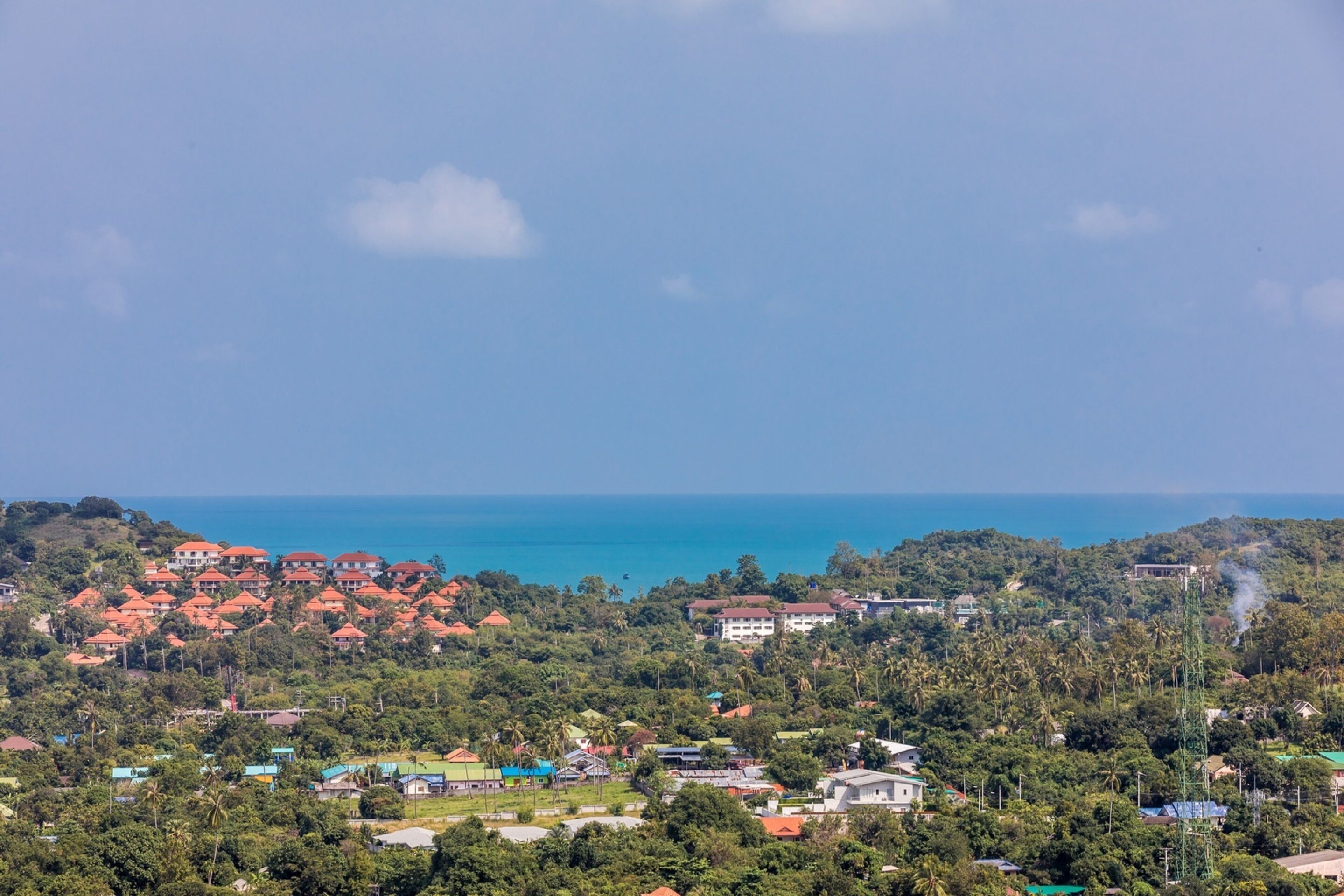 A coastal town with red-roofed buildings, dense greenery, and a view of the sea.