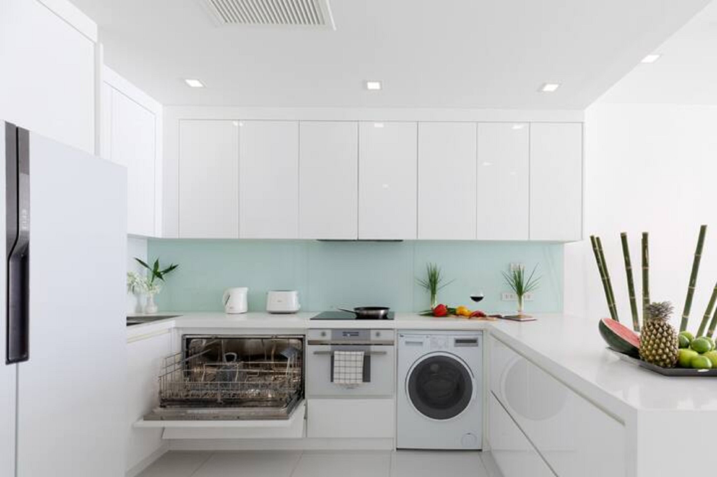 A modern kitchen with white cabinets, a dishwasher, an oven, and a washing machine.