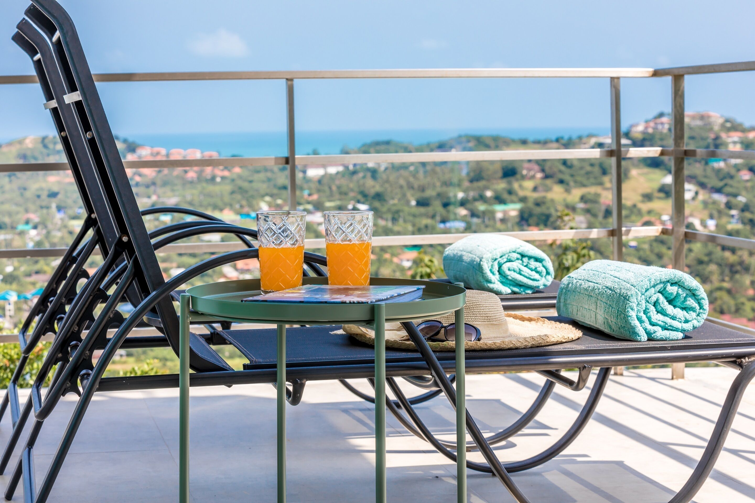 Un balcon avec une table, deux verres de jus d’orange et deux serviettes enroulées.